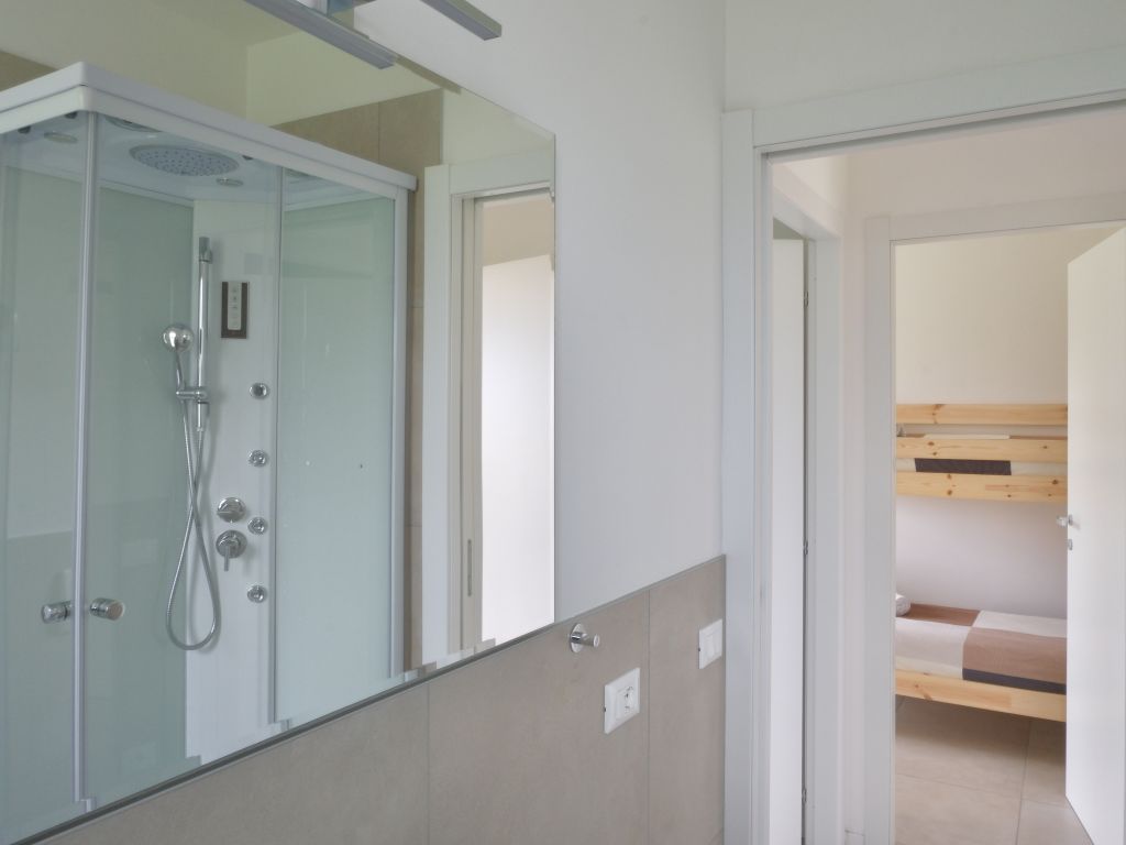 Doccia moderna in bagno con pareti bianche e specchio grande