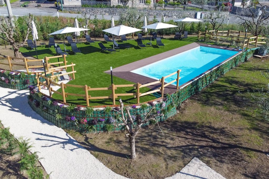 Piscina rettangolare con lettini e ombrelloni su prato verde recintato
