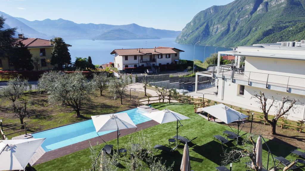 Piscina con ombrelloni e lettini in giardino curato con vista su lago e montagne