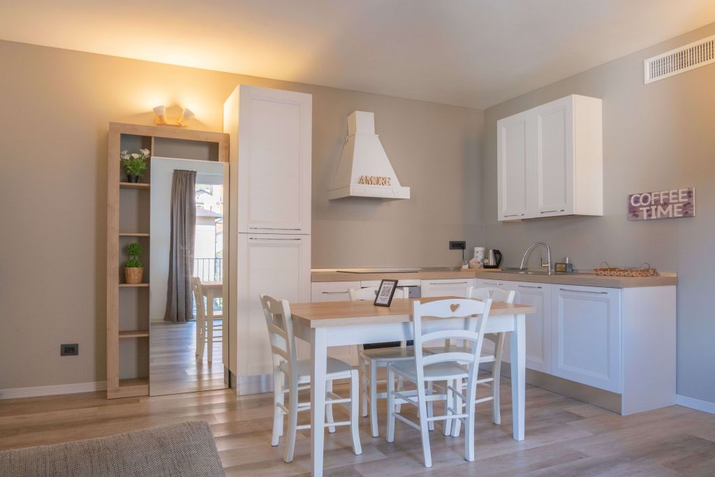 Cucina moderna con tavolo in legno e sedie bianche, mobili bianchi e cappa con scritta Amore