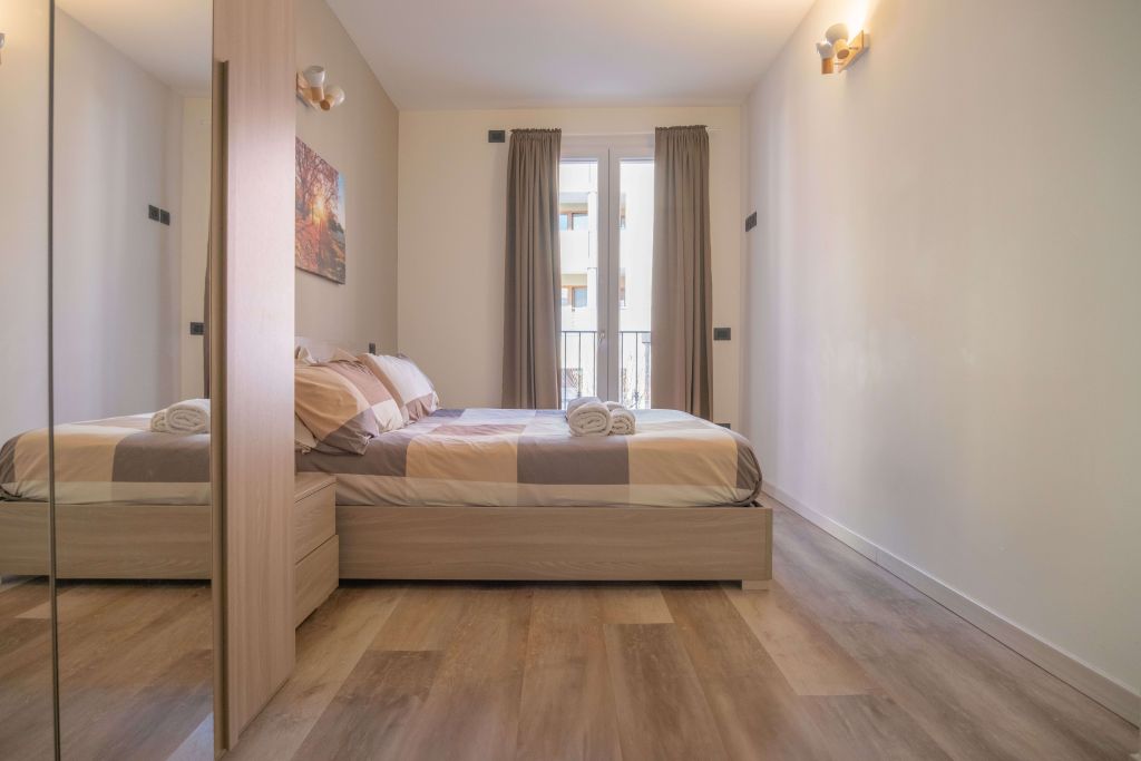 Camera da bed con bed matrimoniale, armadio con specchio e finestra con tende beige.