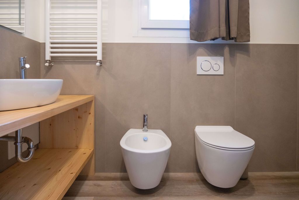 Bagno moderno con lavabo su piano in legno, bidet e wc sospesi, pareti beige e finestra con tenda