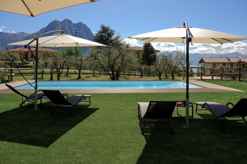 Piscina all'aperto con ombrelloni e lettini su prato verde, montagne sullo sfondo