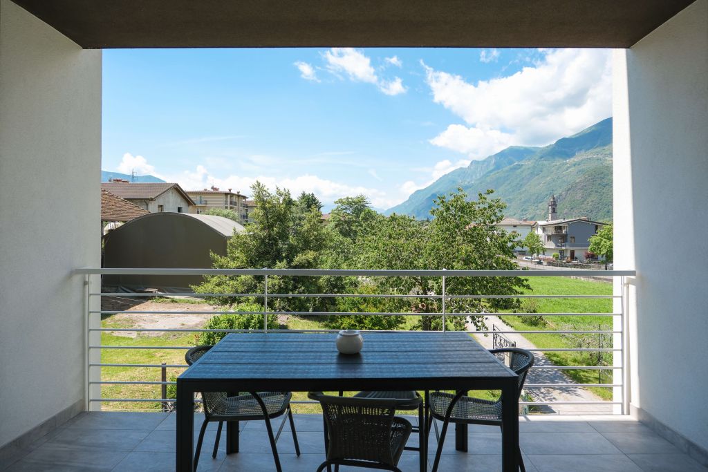 Terrazza con tavolo e sedie, vista su alberi, case e montagne sullo sfondo
