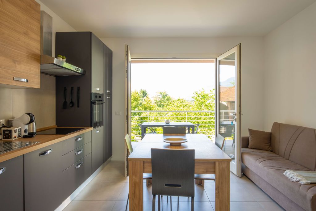 Cucina moderna con tavolo in legno e porta finestra aperta su balcone verde