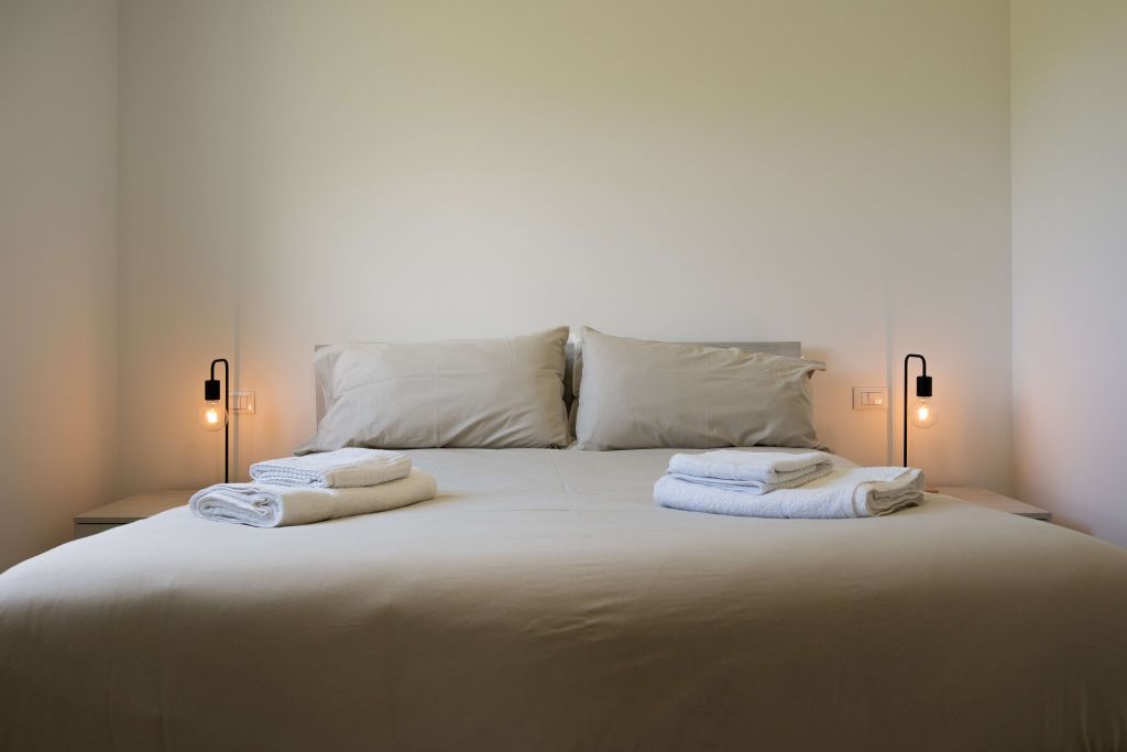 Letto matrimoniale con lenzuola beige e asciugamani piegati, lampade da comodino accese