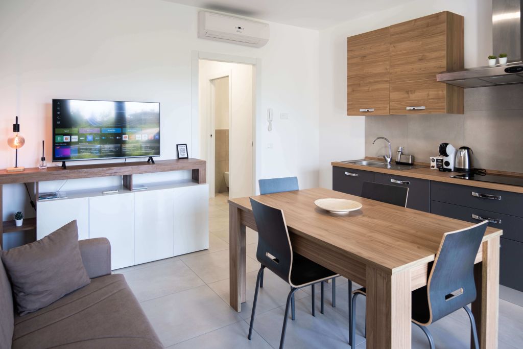 Soggiorno con divano, TV, aria condizionata e cucina moderna con tavolo e sedie.