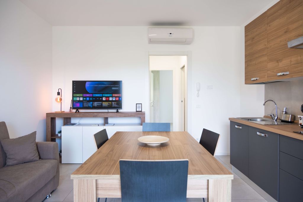 Soggiorno con tavolo in legno, divano grigio, TV e cucina moderna a vista