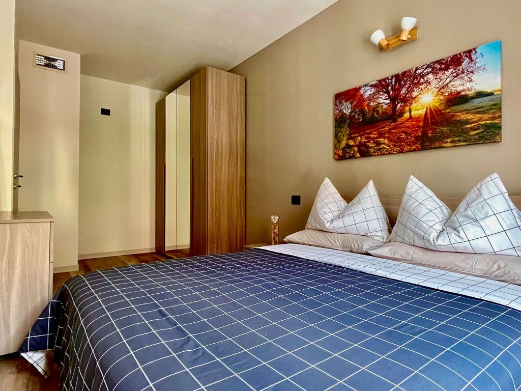 Camera con letto matrimoniale, armadio con specchio e quadro con paesaggio autunnale.