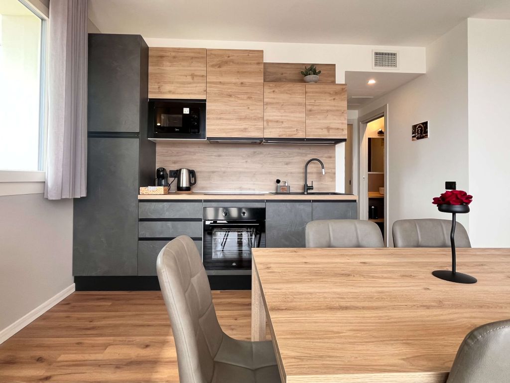 Cucina moderna con mobili in legno chiaro e scuro, elettrodomestici integrati e tavolo in legno con sedie grigie