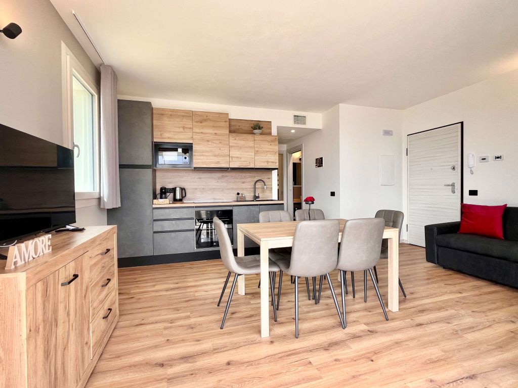Soggiorno con cucina a vista, tavolo con sei sedie, divano nero e mobile con TV