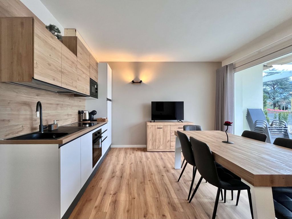 Soggiorno con cucina moderna, tavolo e sedie, tv e porta finestra con vista esterna