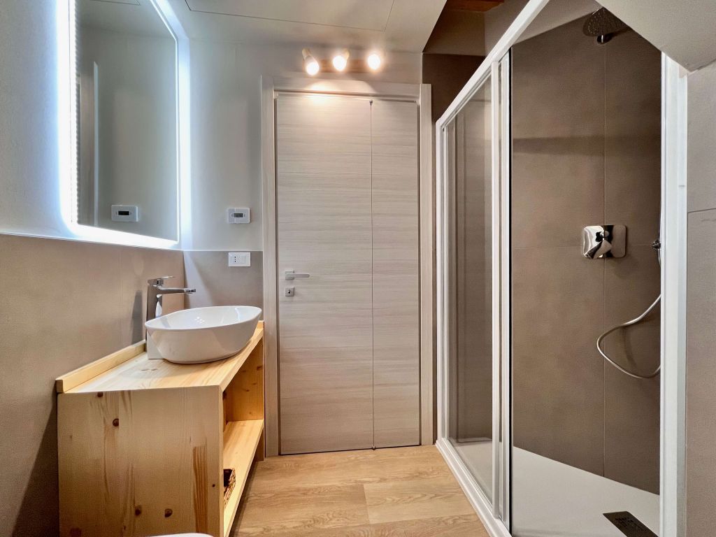 Bagno moderno con lavabo a ciotola, specchio illuminato e doccia con box trasparente
