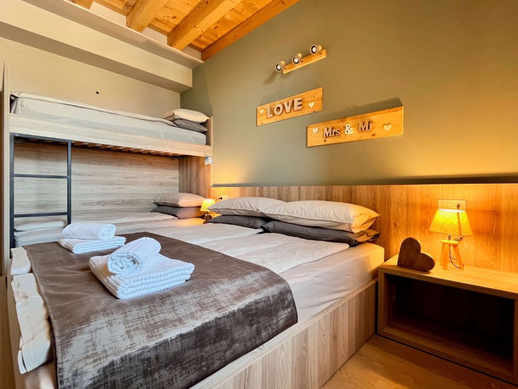 Camera con letto matrimoniale e letto a castello, pareti verdi e soffitto con travi in legno