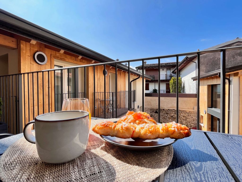 Balcone con tavolo, tazza, dolci e vista su edifici in legno e cielo sereno.