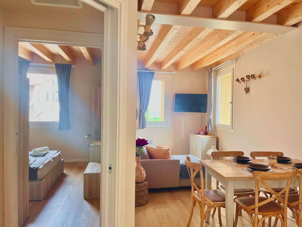 Soggiorno luminoso con travi in legno a vista, divano, TV a parete e tavolo da pranzo in legno.