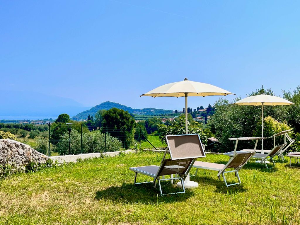 Lettini e ombrelloni in giardino con vista su colline e cielo azzurro