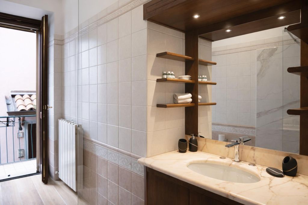Bagno con lavabo in marmo, specchio grande e porta finestra aperta su balcone