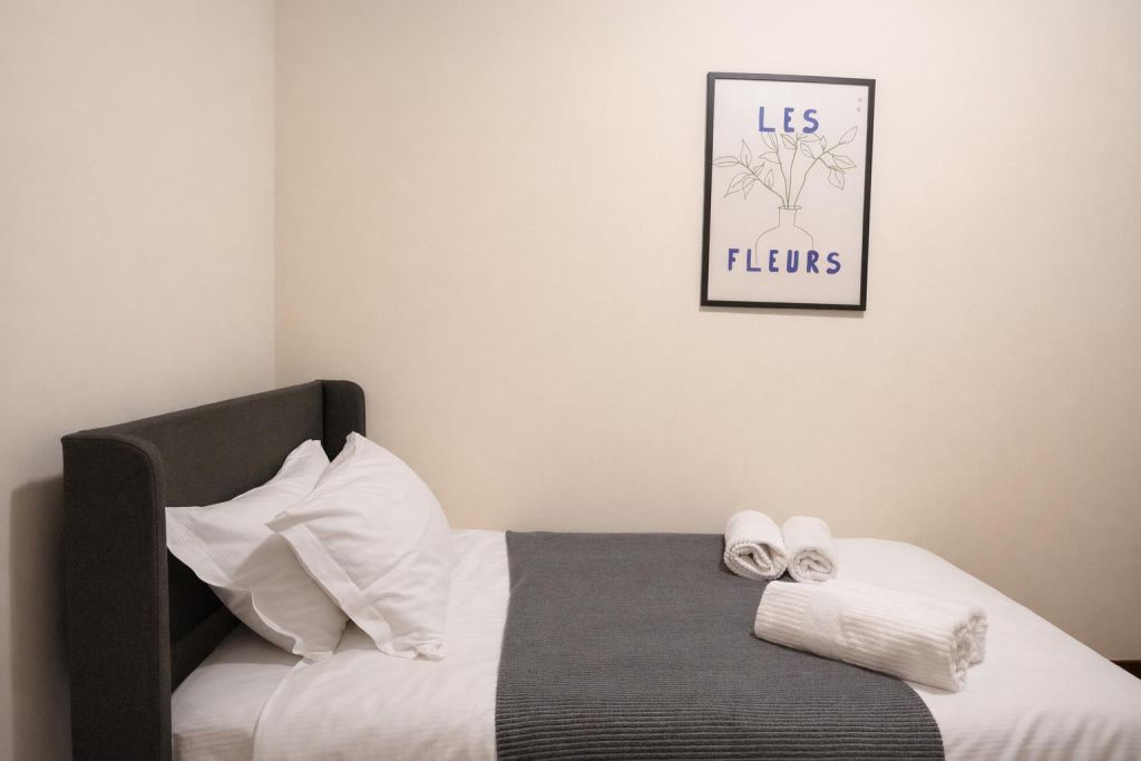 Letto singolo con cuscini bianchi, coperta grigia e asciugamani arrotolati