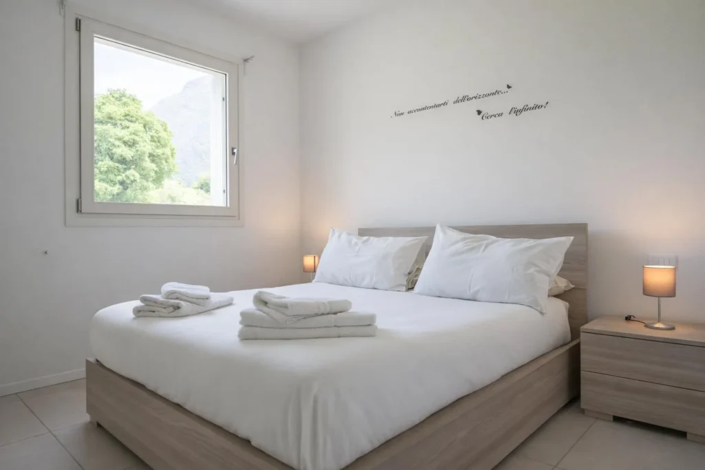 Camera da letto luminosa con letto matrimoniale, lenzuola bianche e finestra con vista su albero e montagna