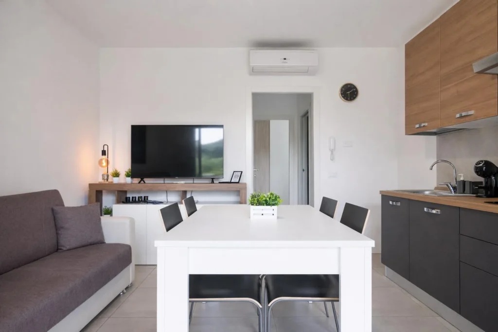 Soggiorno moderno con divano, tavolo bianco, TV e cucina a vista con mobili scuri