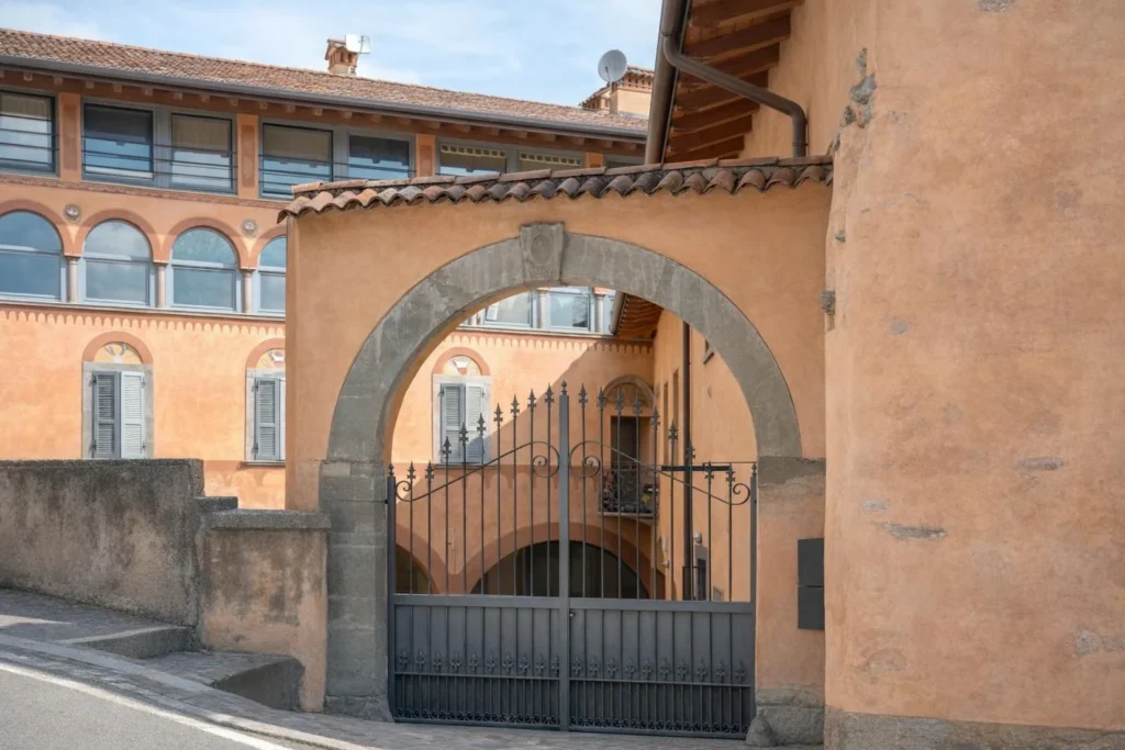 Ingresso esterno con cancello in ferro e arco in pietra su strada in pendenza