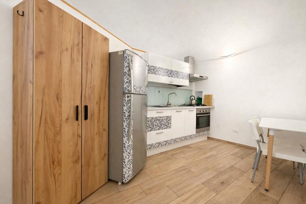 Cucina moderna con mobili bianchi decorati, frigorifero e tavolo con sedie bianche.