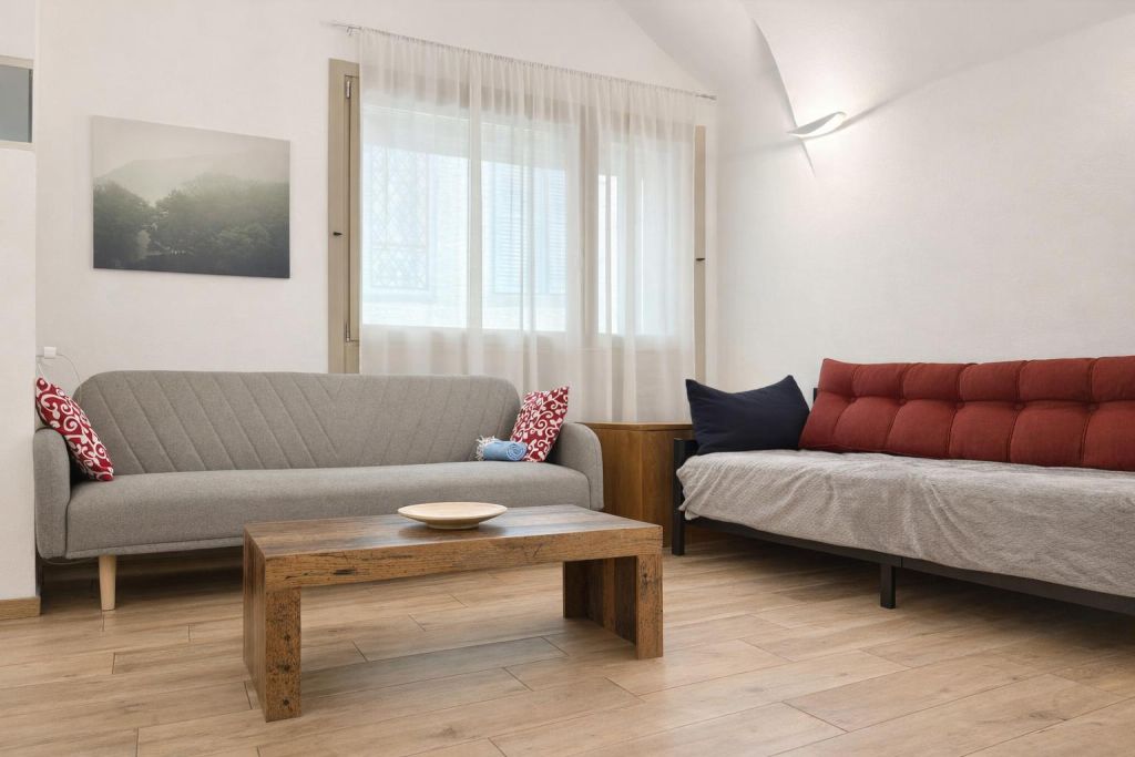 Soggiorno con due divani, tavolino in legno e finestra con tenda bianca.