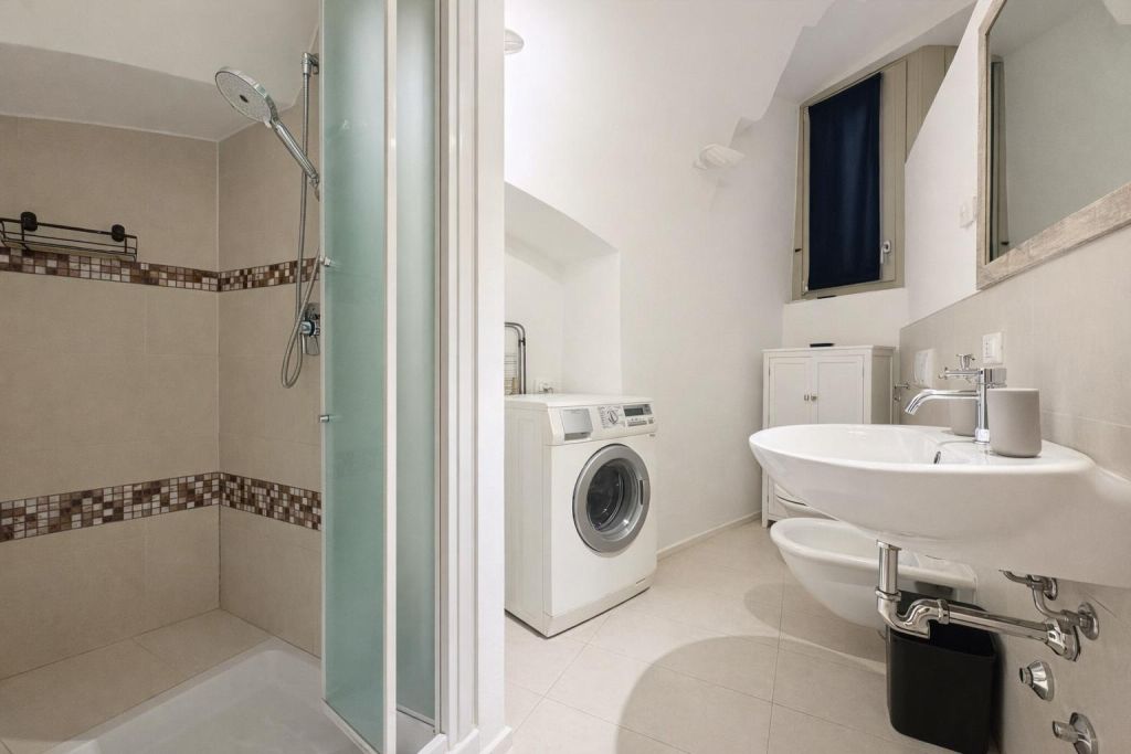 Bagno con doccia, lavandino, bidet, lavatrice e mobiletto bianco sotto finestra