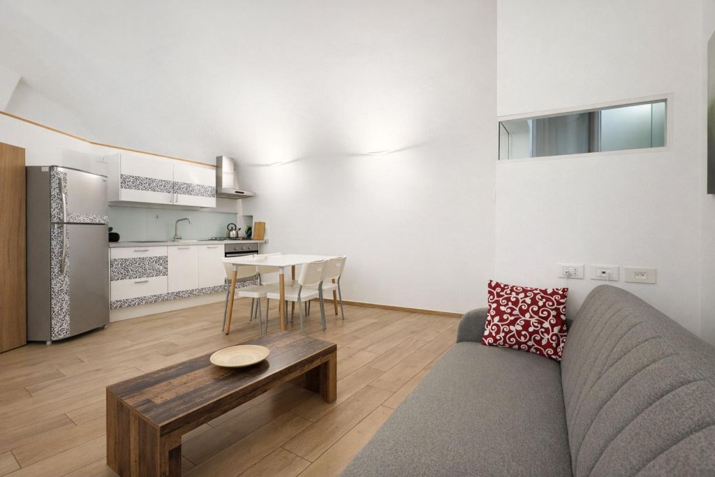 Soggiorno con divano grigio, tavolino in legno e cucina moderna con tavolo bianco e sedie