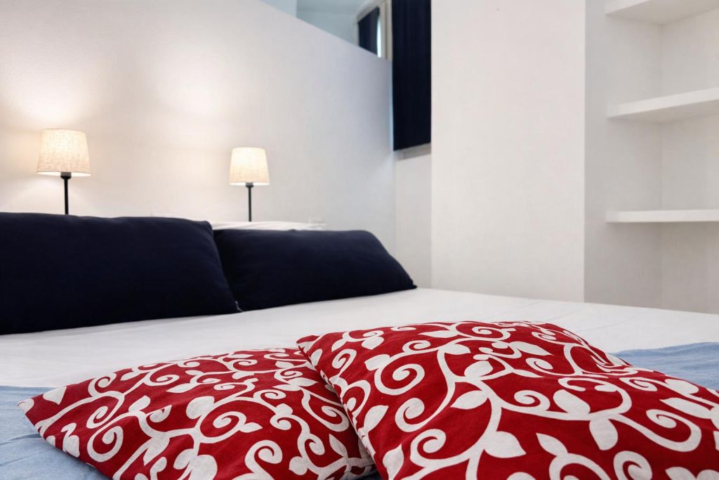 Letto con cuscini rossi decorati e lampade accese su parete bianca