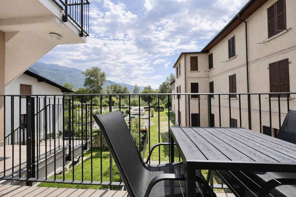Balcone con tavolo e sedie nere, vista su giardino e montagne sullo sfondo.