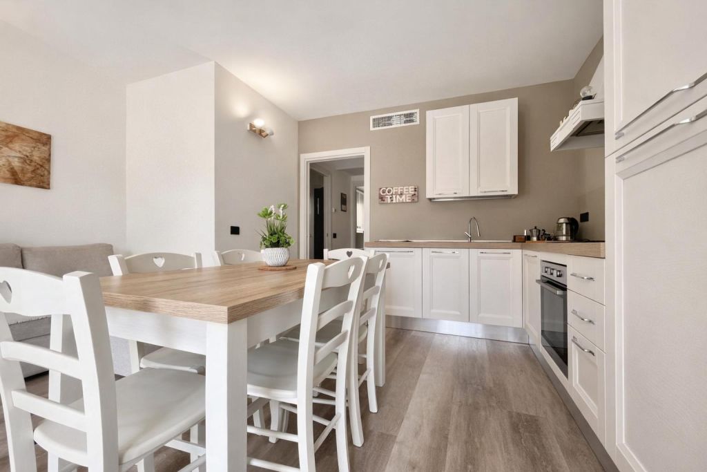 Cucina moderna con tavolo in legno chiaro e sedie bianche, pareti beige e pavimento in legno chiaro