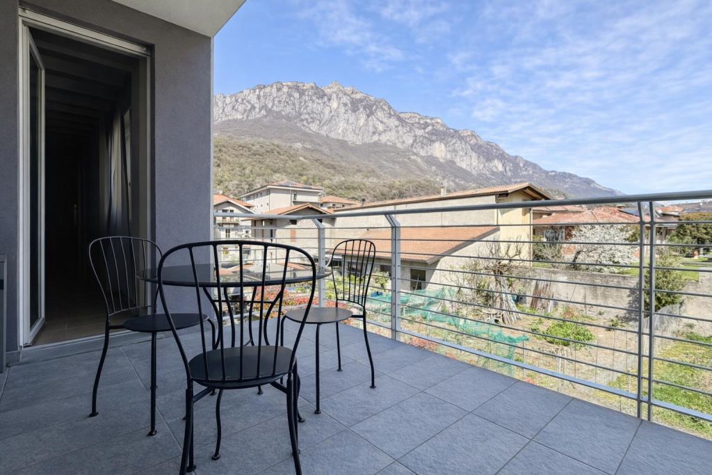 Balcone con tavolo e sedie nere, vista su montagne e tetti di case.