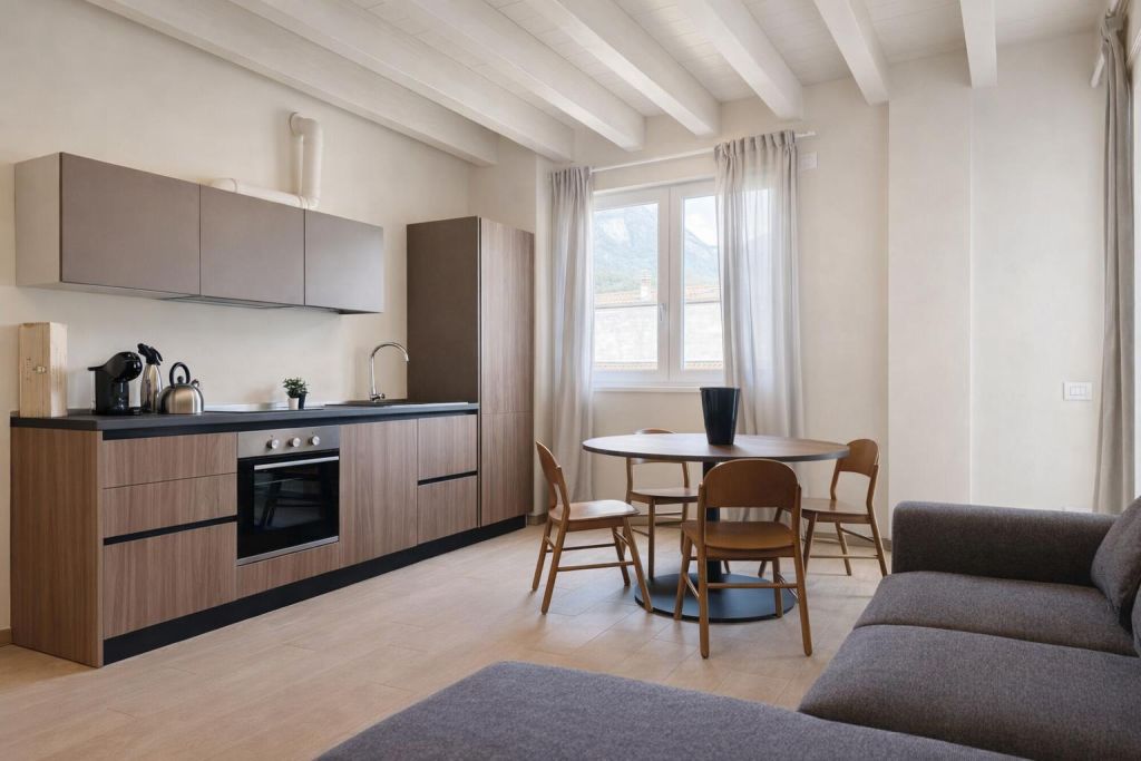 Soggiorno con cucina moderna, tavolo rotondo e divano grigio vicino alla finestra luminosa