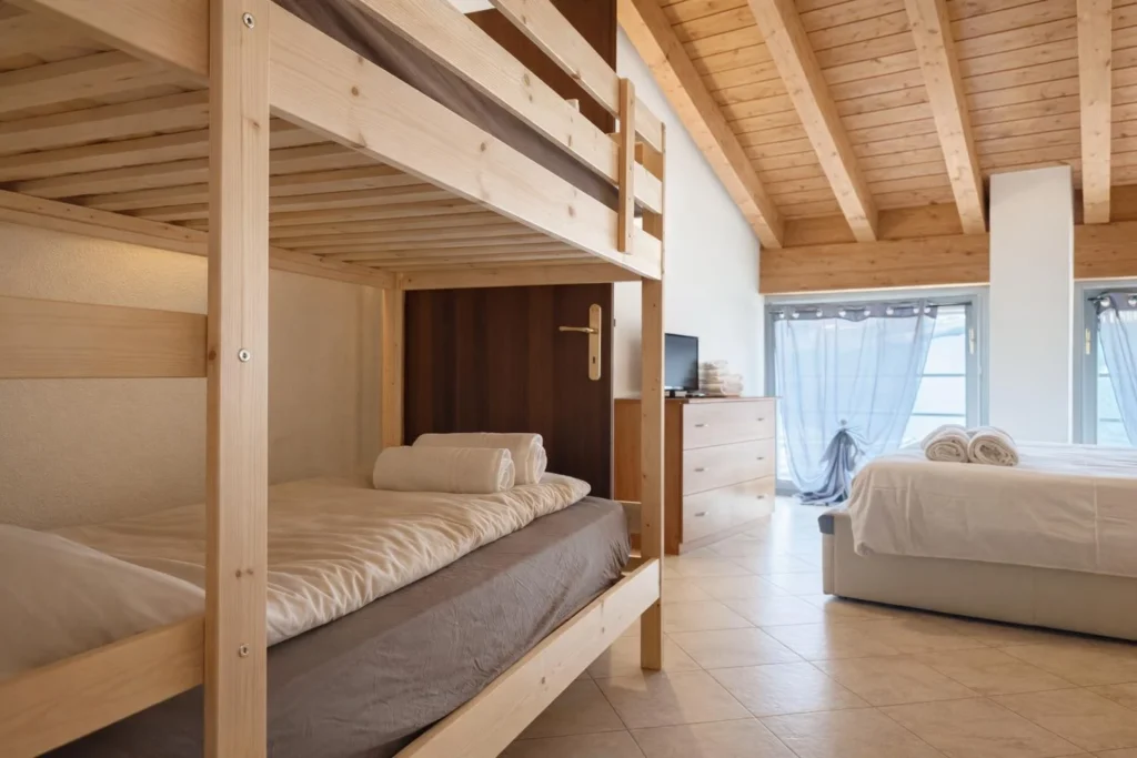 Camera con letto a castello in legno chiaro e letto matrimoniale, soffitto con travi a vista