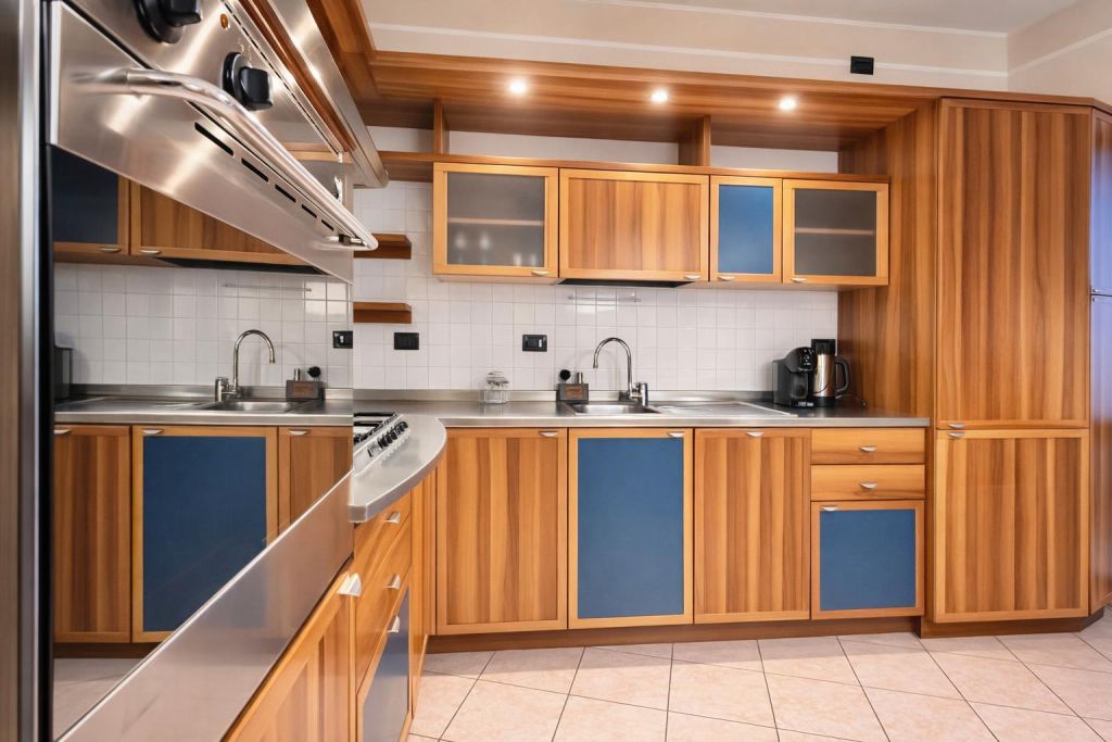 Cucina con mobili in legno e pannelli blu, piano in acciaio e piastrelle bianche a parete.