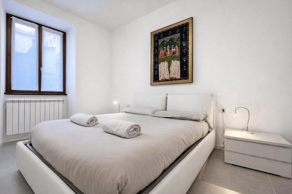 Camera da letto con letto matrimoniale, due asciugamani arrotolati e quadro decorativo