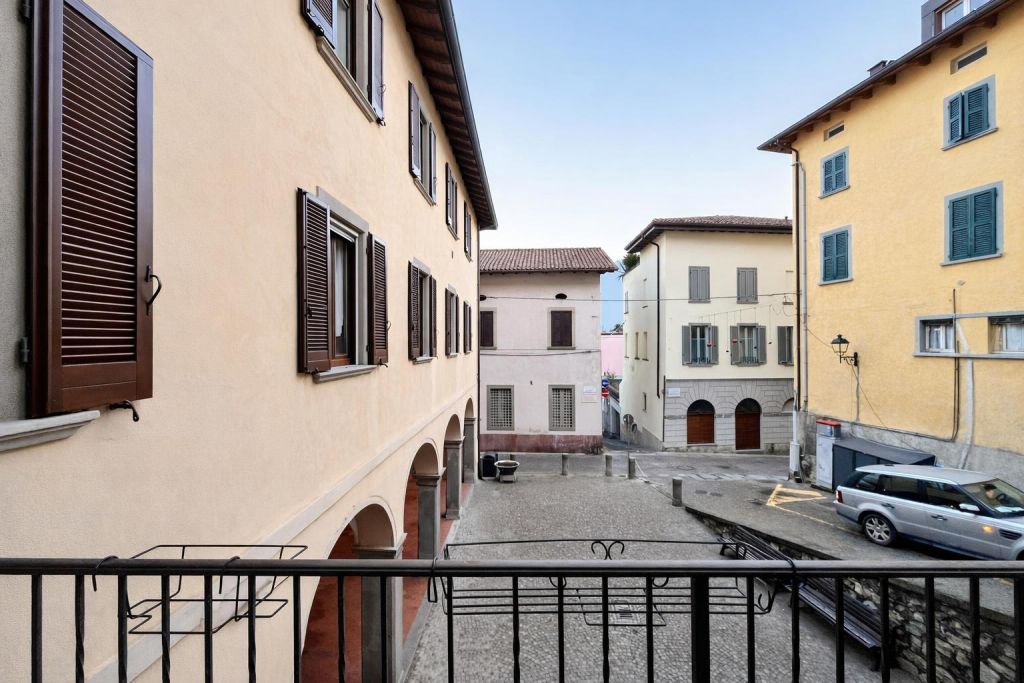 Vista da balcone su piazza con edifici storici e auto parcheggiata