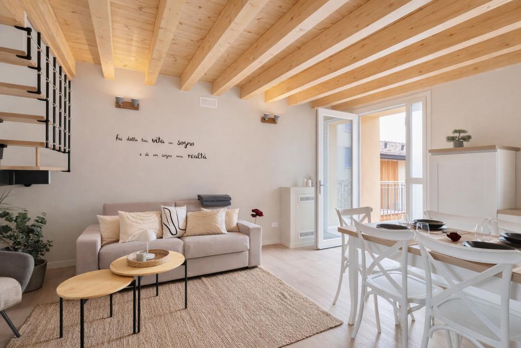 Soggiorno luminoso con divano beige, tavolini in legno e tavolo da pranzo bianco vicino a porta finestra aperta