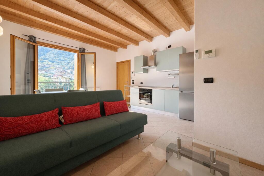 Soggiorno con divano verde e cucina moderna, finestra aperta con vista su montagna