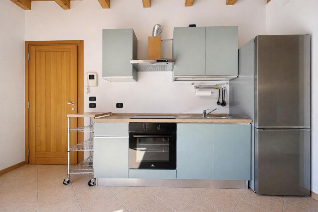 Cucina moderna con mobili azzurri, forno nero, frigorifero acciaio e porta legno.