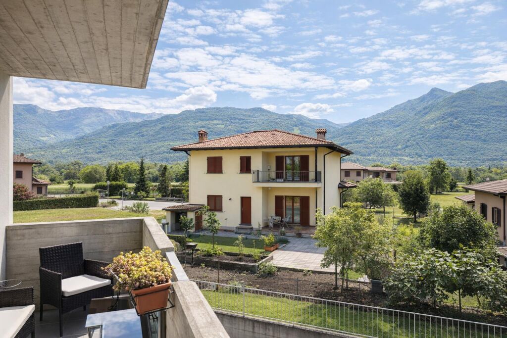 Balcone con sedie e tavolino, vista su giardino e casa con montagne sullo sfondo